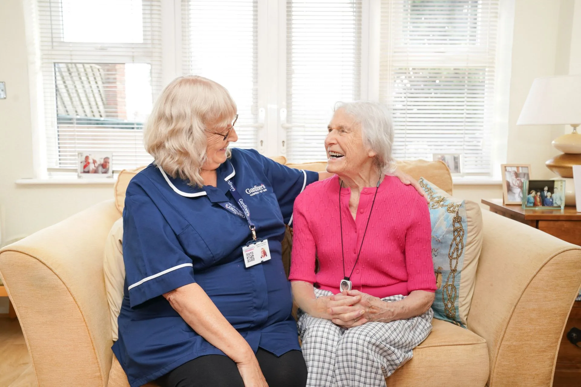 A Gardiner's carer and a long-standing client laughing together on the sofa at home