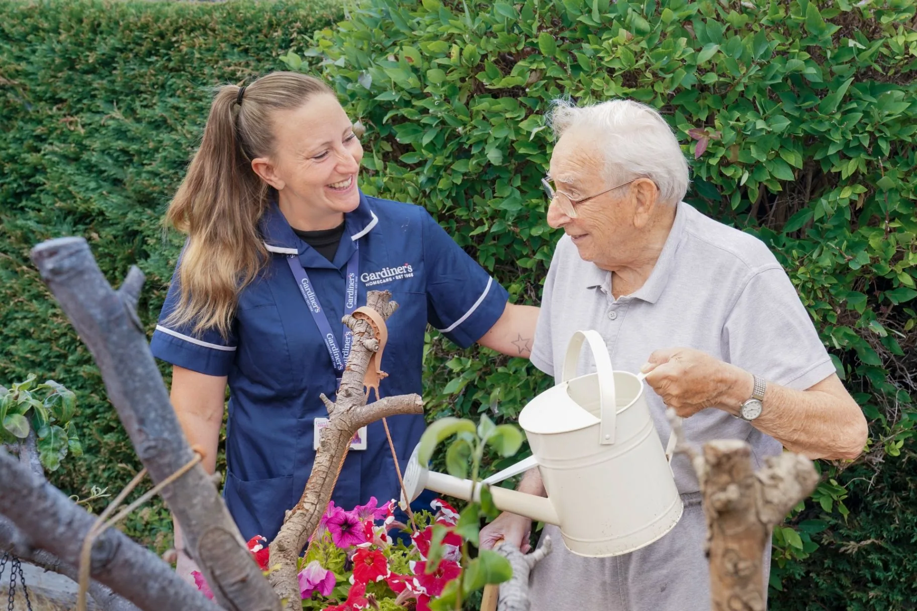 A Gardiner's carer in the garden with an elderly client, sharing a quiet moment as he waters the flowers